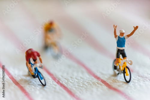 Miniature Cyclists Representing Corporate Success and Financial Growth with the leader raising his arms in victory
