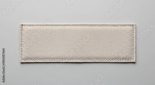 Blank Rectangular Beige Fabric Label With Detailed Stitching on a Light Grey Background, Showcasing Woven Texture for Design Mockups and Textile Projects