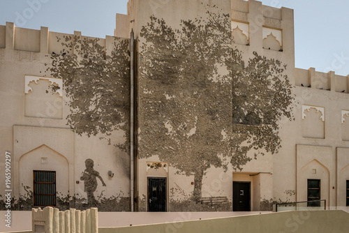 Mural of child and tree painted on beige traditional building wall in Doha Qatar