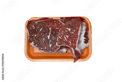 Frozen raw beef steaks in orange plastic tray pack isolated on white. Top view of frozen red meat steaks showing ice crystals and freezer burn in a supermarket container. Ideal for food safety, preser