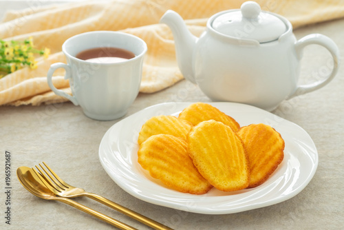 Madeleine on white plate and cup of tea