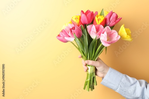 Woman with bouquet of aromatic bright tulips on yellow background, closeup. Space for text
