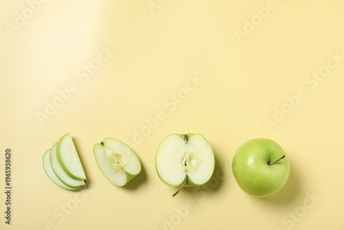 Whole and cut fresh apples on pale yellow background, flat lay. Space for text