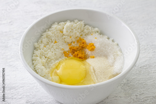 Ingredients for ricotta cheese filling in white bowl with raw egg orange zest semolina and sugar on kitchen table