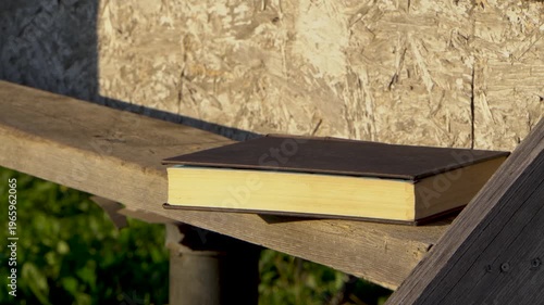 A book on a wooden step. A man's hand picks up and puts down the book. Close-up. Solitary reading. A large book. Outdoors. A country house.