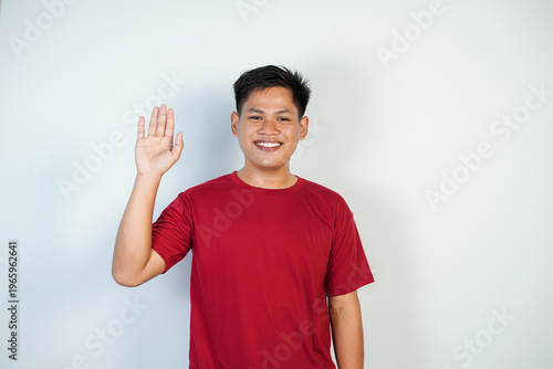 Smiling Young Asian Man Waving Hello in Casual Red Shirt Studio Portrait for Greeting and Friendly Vibes