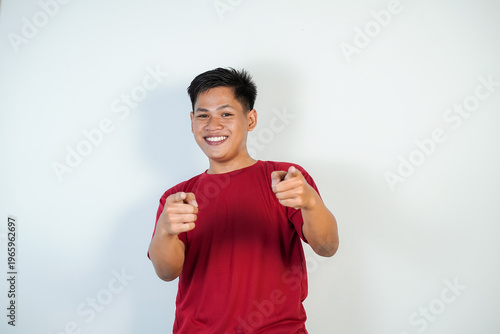 Smiling Young Asian Man in Red T-Shirt Pointing at Camera Confident Friendly Casual Portrait on White Background
