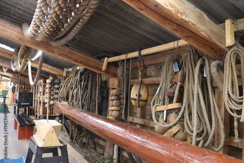 Traditional shipbuilding workshop with ropes and maritime tools hanging on wall.
