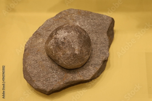 Stone with embedded metal sphere artifact displayed on museum background.