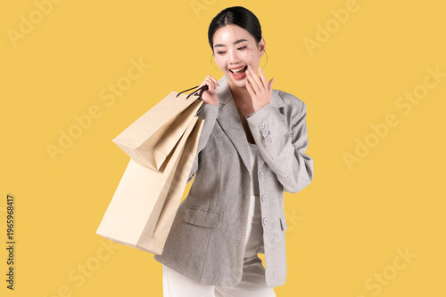 Happy young Asian woman holding shopping bags on yellow background, for discount clothes and mid year sale concept. women glamour lifestyle in holiday.