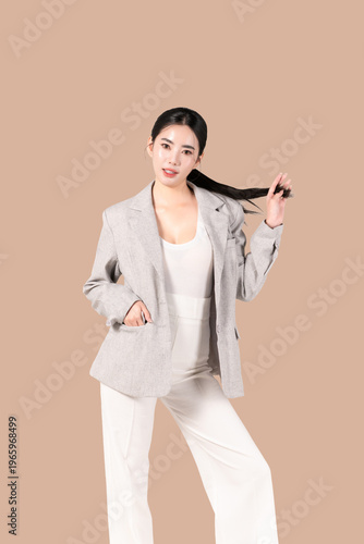 Confident young Asian woman with smooth skin and healthy long hair posing isolated on beige background for beauty, skincare and self confidence concept.