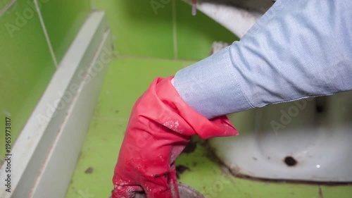 Cleaning clogged drain hole under toilet with hand, Plumber cleaning a clogged sewer drain hole in the bathroom floor.
