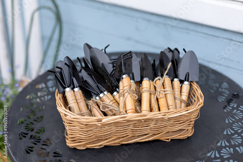 Wallpaper Mural Wicker basket filled with small gardening tools placed on a metal table outdoors, representing home gardening, planting, and garden care concept, seasonal garden work, hobby and leisure Torontodigital.ca