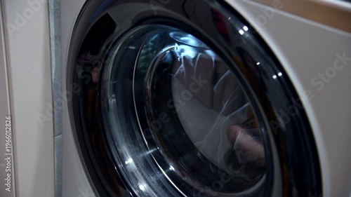 Close-up of closing the door washing machine door with clothes, hand touching glass surface
