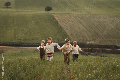 Four children running across countryside field holding hands, laughing in warm summer light, carefree childhood joy, rustic lifestyle, freedom and happiness, natural candid moment
