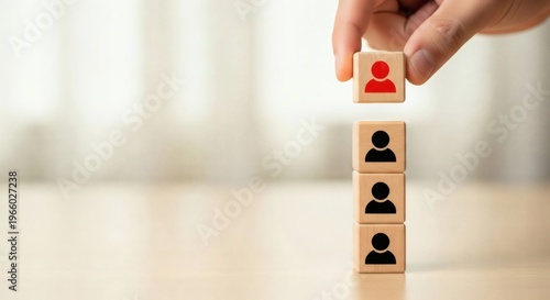 Leadership and Team Promotion Concept. Hand placing wooden cube with red person icon on vertical stack of team blocks, representing career growth and leadership development.
