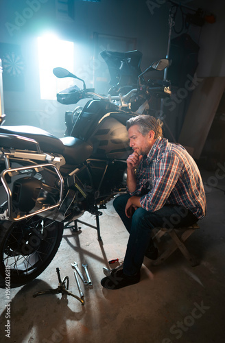 Obraz na płótnie A man is sitting near a motorcycle in a garage