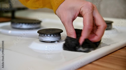 Hand scrubbing gas stove burners with sponge in bright kitchen setting