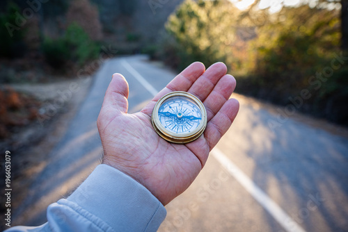Canvas Print Hand holding a compass on a diverging road, finding direction and making a decis