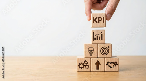 Hand placing a wooden block with kpi text on top of a pyramid of blocks with business icons