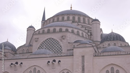 Close view of a mosque dome with detailed Islamic architecture and a tall minaret against a cloudy sky. The structure represents religious design, symmetry, and cultural heritage.