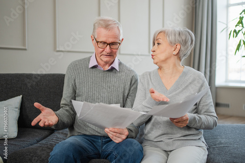 Sad tired disappointed middle aged senior couple sit with paper document. Unhappy older mature man woman reading paper bill managing bank finances calculating taxes planning loan debt pension payment