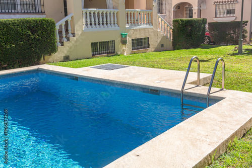 Swimming pool with ladder and blue water in sunny backyard