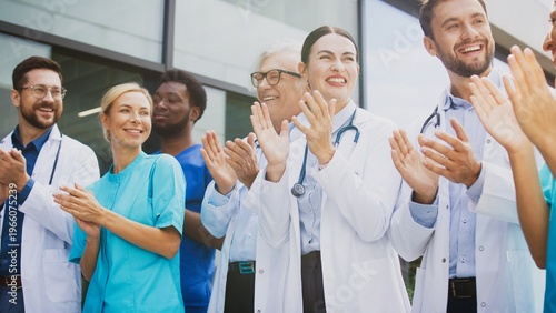 Foto Smiling medical staff clapping hands while standing outside clinic under bright daylight