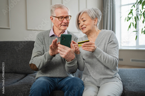 Senior couple man woman shopping online with smartphone paying with credit card. Old people buying on Internet enter credit card details at home indoors. Online shopping delivery service ecommerce