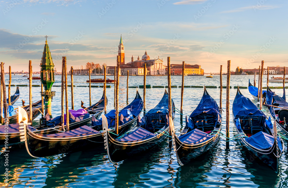 Fototapeta premium row of parked venetian gondola boats in Grand canal of Venice. Beautiful sunset or sunrise landscape with gondolas in blue water of Venice.