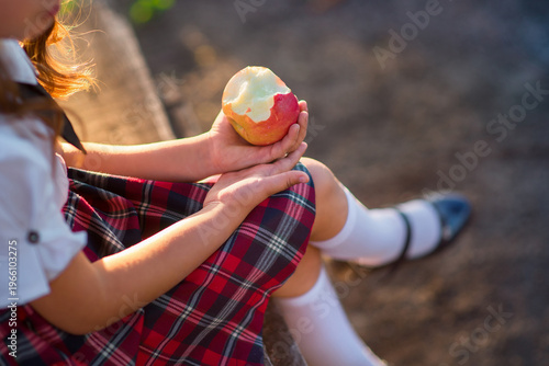 Schoolgirl sitting outdoors and holding a bitten red apple in her hands