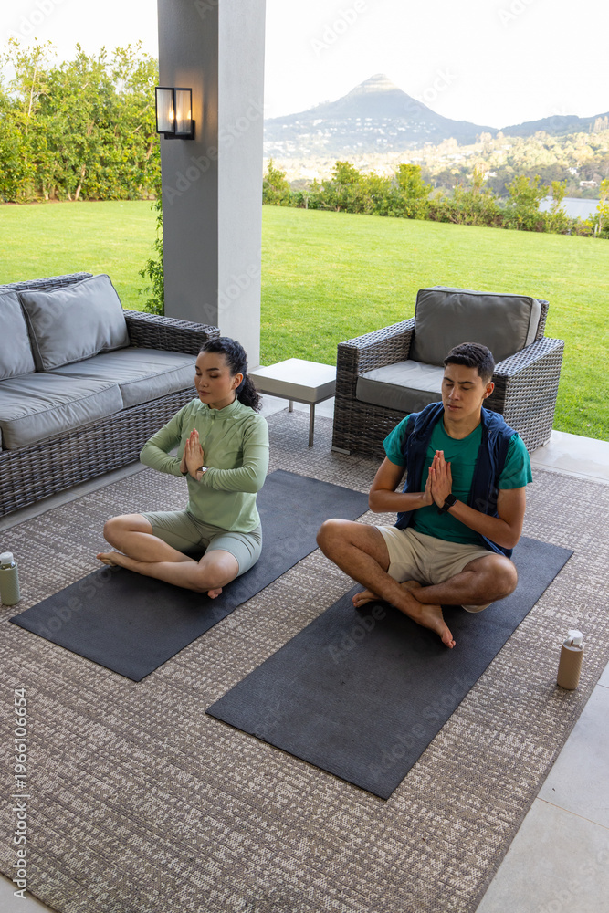 Fototapeta premium Couple meditating cross-legged on patio wearing activewear on yoga mats with water bottles
