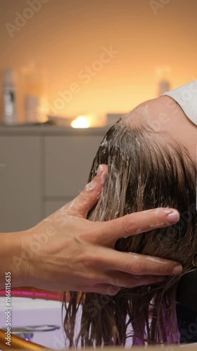 Professional hairstylist applying treatment and shampooing a female client's hair in a beauty salon