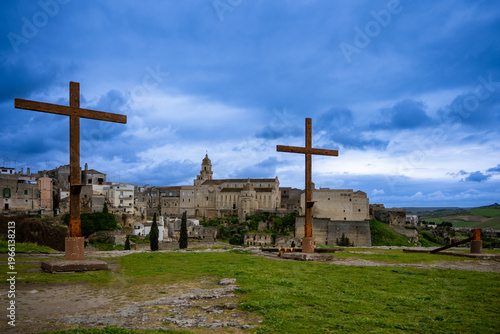 Wooden three crosses (with fallen one) on a hill in middle ages town with a heavy blue rainy sky - crucifixation on catholic Easter