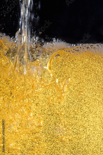 Beer. Jet of beer is poured into a beer glass, causing a lot of bubbles and foam. Beer background