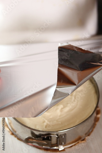 Covering baking pan with foil before and place to fridge. Making frozen strawberry cheesecake series.