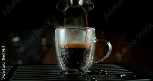 Fresh espresso pouring from coffee machine into glass cup with rich crema and rising steam. Warm cinematic scene capturing preparation of black coffee in cozy atmosphere.