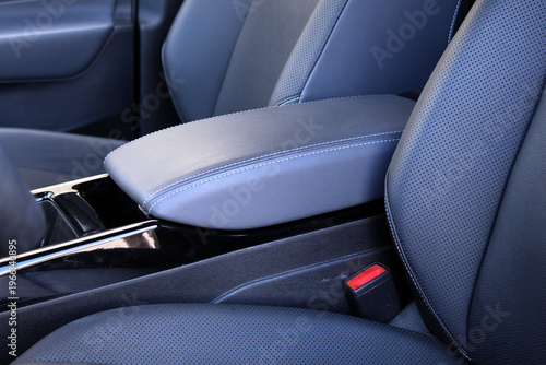 Close-up of light gray perforated leather center armrest in premium car. Premium car interior with comfortable seats.