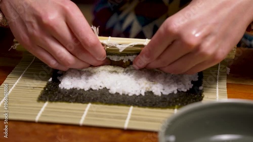 Homemade sushi roll nori algae getting wetted and closed by hands horizontal