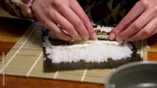 Female hands are cutting a sushi roll with nori algae seaweed and rice on a chopping board with a sharp knife. Different healthy ingredients are enclosed in the Japanese food roll. Healthy homemade fo
