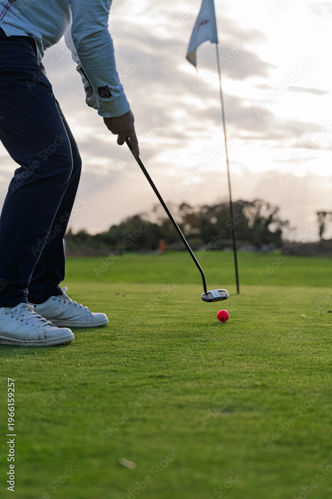 Obraz premium Golfer Preparing a Putt on Green at Sunset with Red Ball