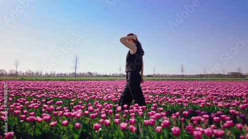 Woman walks through rows of colorful tulips in open field, slow movement across flowers, springtime outdoor activity, relaxed lifestyle, nature exploration.