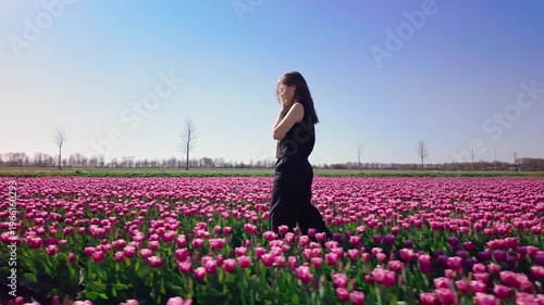 Woman stands and poses among blooming tulips, turning slightly in field, expressive outdoor lifestyle moment, spring season, floral landscape 