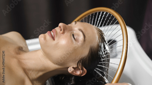 Young woman receiving anti-stress scalp massage under gentle water stream in Japanese spa.
