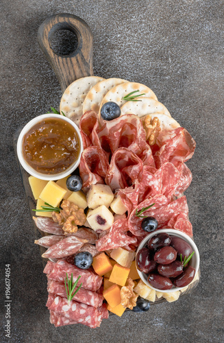 Antipasti charcuterie board with cured meats, cheeses, crackers, fig jam, walnuts. Top view on rustic background.
