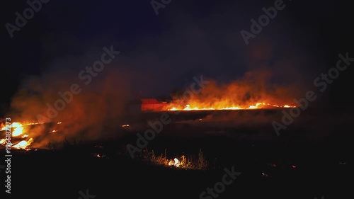 Bright fire burns across dry farmland. Thick smoke and glowing flames light the night. Climate change and environmental disaster theme. Rural wildfire scene.