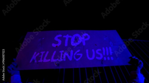 Handheld cardboard sign reading “Stop killing us” at public protest. Emotional message against violence. Civil unrest and anti violence movement. Social crisis awareness concept.