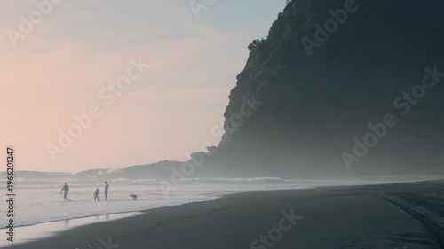 A family enjoys the surf at Karekare, Auckland, New Zealand. They are enjoying the waves and the beautiful scenery of the Ocean.