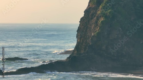 Waves crash against the rugged cliffs of Karekare Beach, New Zealand. The wild, untamed beauty of the coastline is a popular destination for surfers.