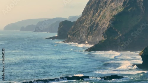 Waves crash against the rugged cliffs and sea stacks of Karekare Beach, New Zealand. The wild, untamed beauty of the coastline is a popular destination for surfers.
